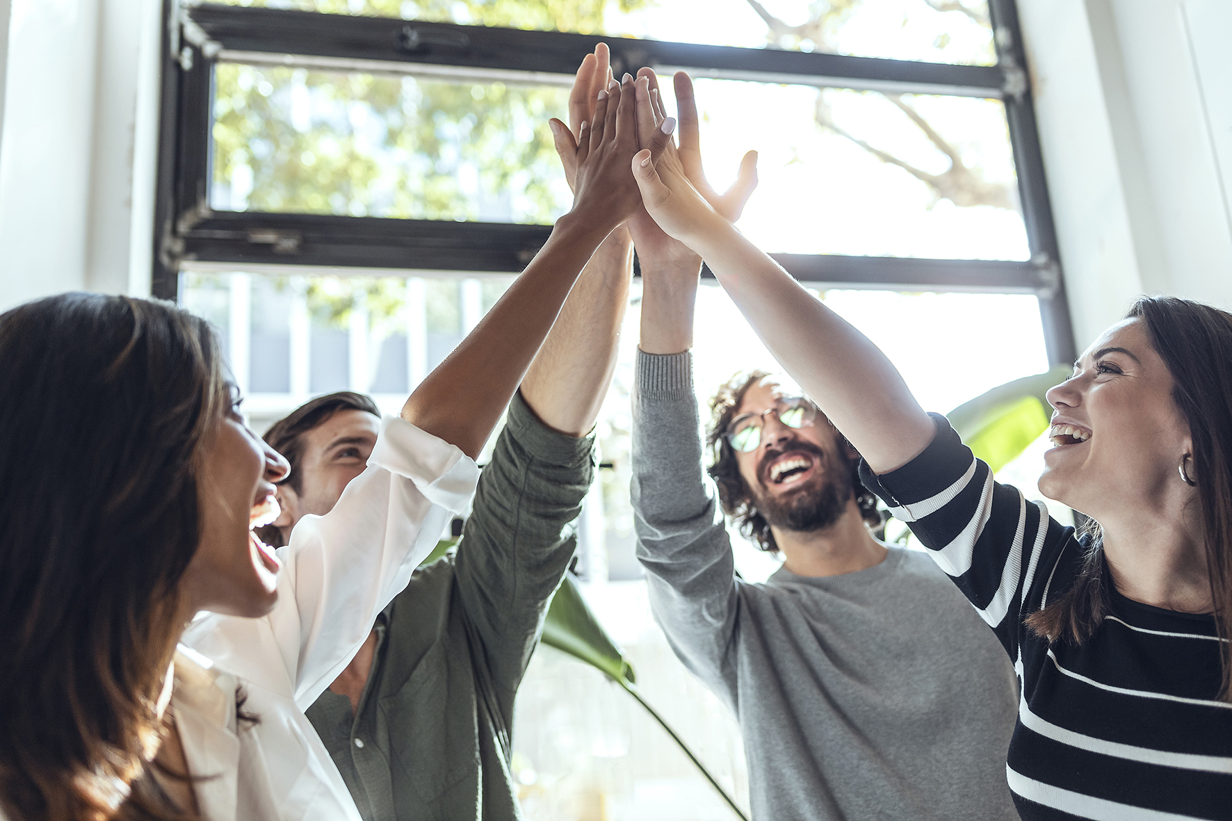 Vier Personen die sich ein HighFive geben; Symbol für erfolgreiche Arbeit